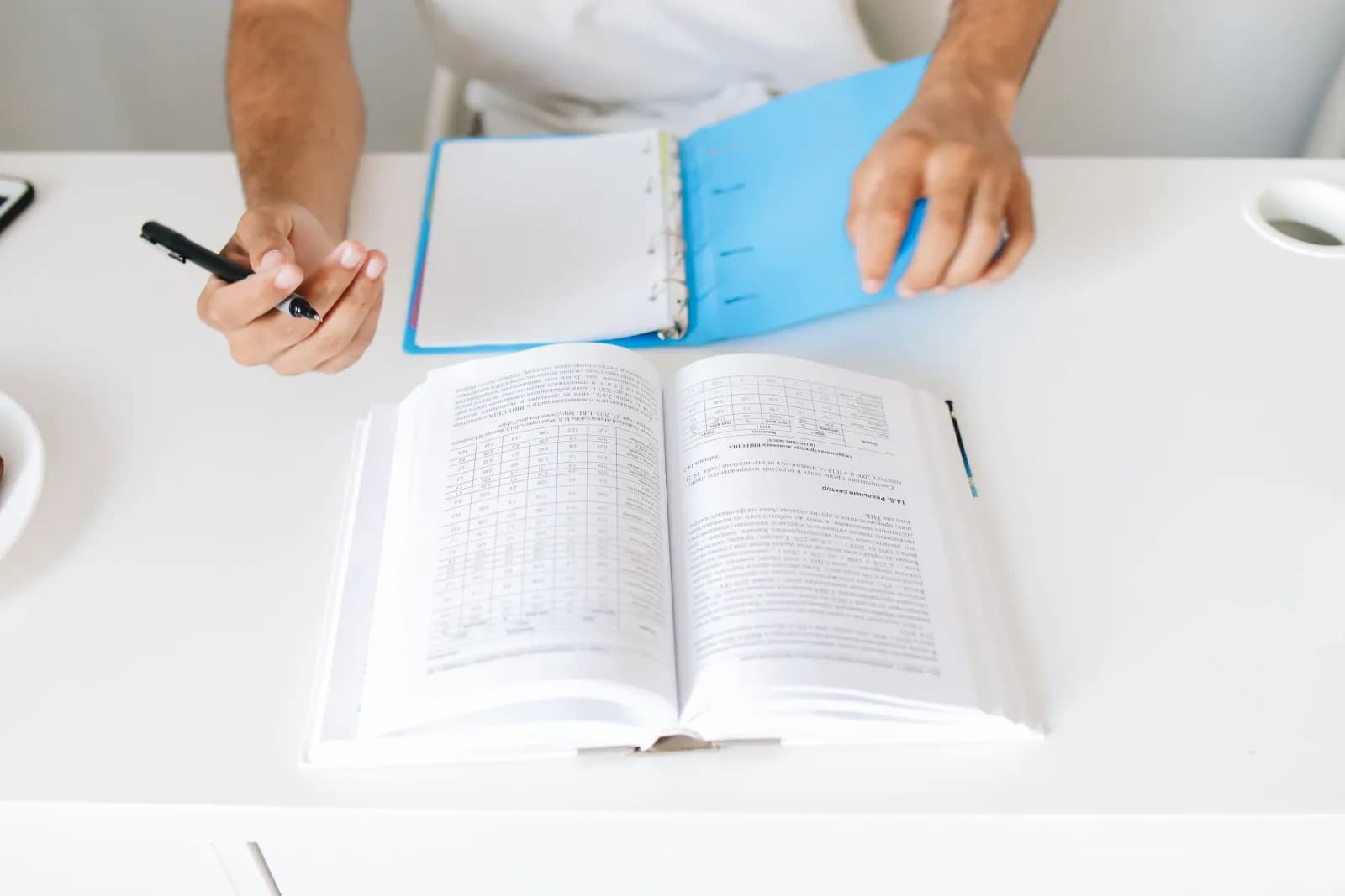 An open textbook, a ring binder and a pen laid out to plan a study schedule