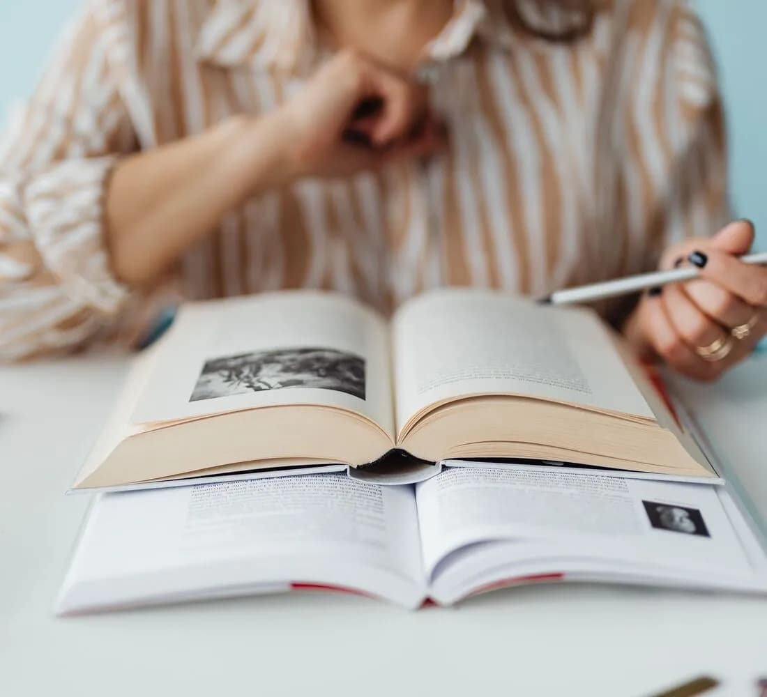 A student pausing over an open textbook with a hand resting near their face