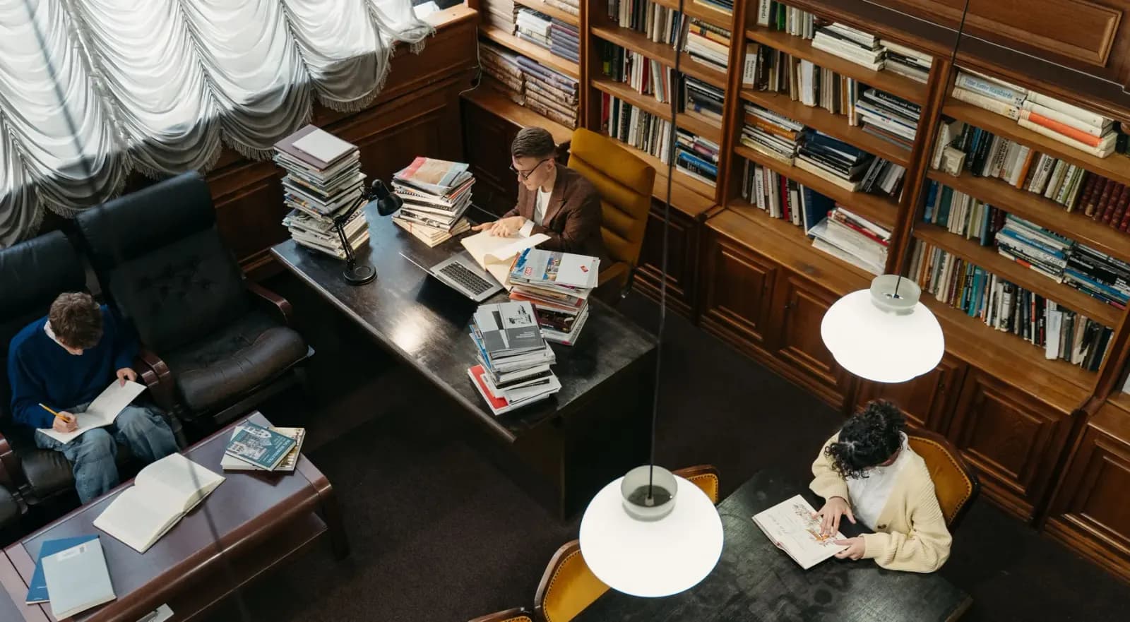 Students studying with textbooks and a laptop at desks in a library